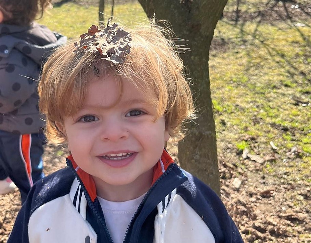 Un bambino sorride all’aperto con una foglia secca tra i capelli